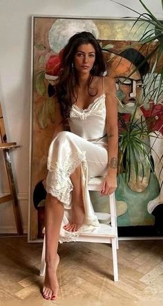 Woman in a white slip dress sitting barefoot in an indoor setting