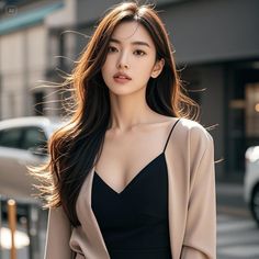 Woman with long hair wearing a black dress and beige jacket outdoors