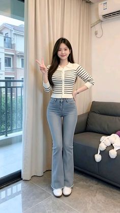 Woman in a striped top and flared jeans making a peace sign indoors