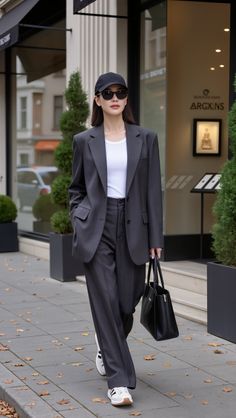 Woman in a dark suit, baseball cap, and sunglasses walking on a street