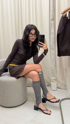 Woman in a brown dress and knee socks taking a mirror selfie indoors