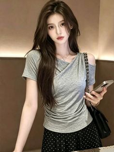 Woman with long hair wearing a gray top and polka dot skirt, holding a phone