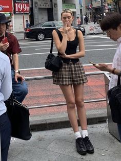 Woman in a plaid skirt and black top smoking on a city street