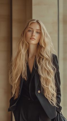 Woman with long blonde wavy hair wearing a black blazer and a necklace
