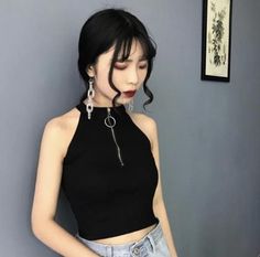 Woman with black hair and dark lipstick wearing a black crop top and chain earrings