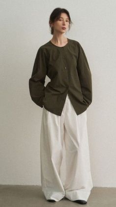 Woman in a dark green shirt and white wide-leg pants against a neutral background