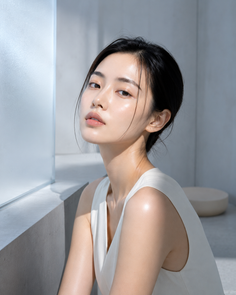 Woman with black hair in a white top, illuminated by soft lighting indoors