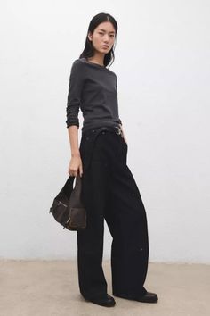 Woman in a dark long-sleeve top and wide-leg pants holding a shoulder bag