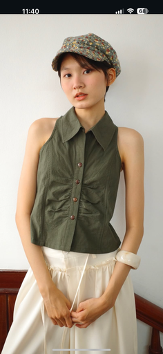 Woman in a floral hat and green sleeveless top against a white wall