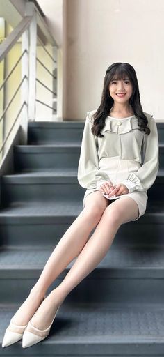 Woman with long dark hair wearing a ruffle blouse and mini skirt, sitting on stairs