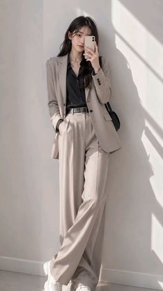 Woman in a beige suit and black shirt taking a mirror selfie