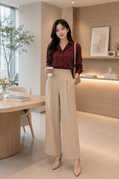 Woman in a maroon shirt and wide leg pants holding a coffee cup indoors
