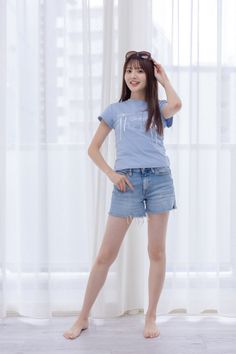 Woman in a light blue t-shirt and denim shorts standing barefoot indoors