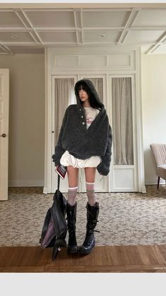 Woman in an oversized dark hoodie and black boots indoors