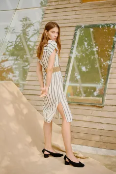 Woman in a striped dress and black shoes posing outdoors against a wooden wall
