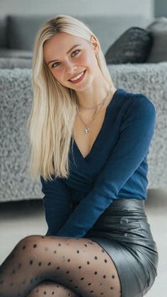 Blonde woman in a blue top and leather skirt with polka dot tights, smiling indoors