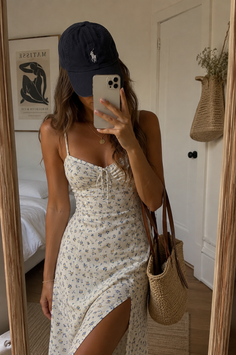 Woman in a floral dress and baseball cap taking a mirror selfie