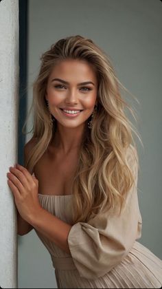 Blonde woman in an off-shoulder dress smiling and leaning against a wall