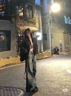 Woman in a crop top and wide leg jeans standing on a street at night