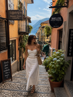 Woman in a white outfit walking down a cobblestone street with a lake and mountains in the background