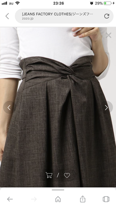 Woman wearing a brown high-waisted pleated skirt with a knot detail and a white top