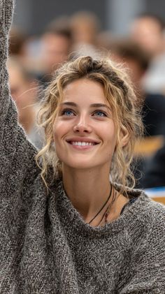 Woman with curly blonde hair and blue eyes smiling and raising her hand