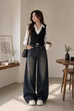 Woman in a black vest and wide leg jeans holding a coffee cup indoors