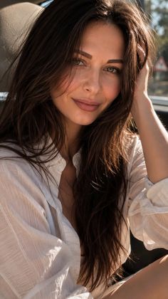 Woman with long brown hair wearing a white shirt, smiling in soft outdoor light