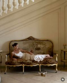 Woman in a slip dress reclining on an ornate sofa in a classic interior