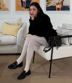 Woman in a black blazer and white patterned tights sitting on a white sofa
