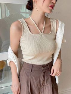 Woman in a ribbed tank top and brown pants with a white shirt draped over her shoulders
