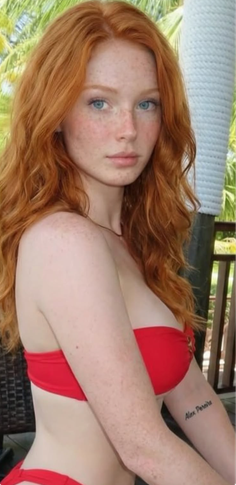 Woman with red hair and freckles wearing a red bikini outdoors