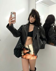 Woman in a leather jacket and mini skirt taking a mirror selfie