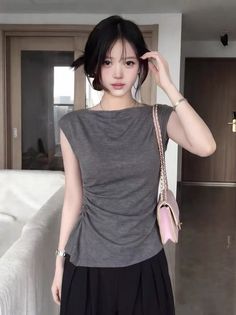 Woman with black hair wearing a gray top and black skirt, holding a pink handbag