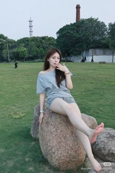 Woman with long hair in an off-shoulder top and denim shorts sitting on a rock in a park
