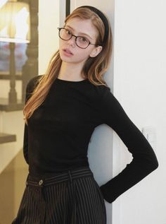 Woman with long hair and glasses wearing a black top and striped pants indoors