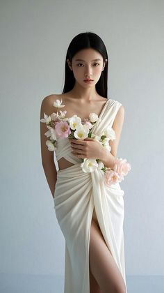 Woman in a white draped dress holding flowers, with a high leg slit