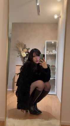 Woman with long black hair taking a mirror selfie while squatting indoors