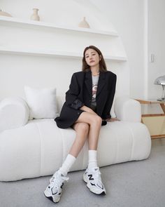 Woman in a black blazer and sneakers sitting on a white couch indoors