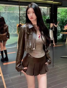 Woman with long black hair wearing a leather jacket and pleated skirt indoors