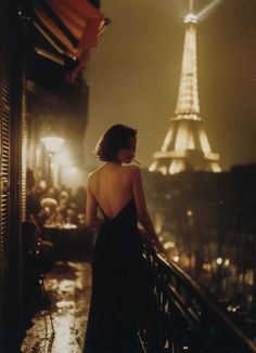 Woman in a backless dress on a balcony overlooking the Eiffel Tower at night