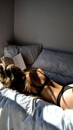 Woman in black lingerie lying on a bed with a book, bathed in soft light