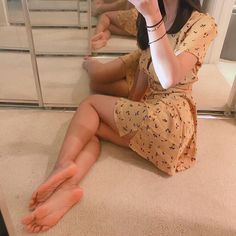 Woman in a yellow floral dress sitting on a carpeted floor with bare feet