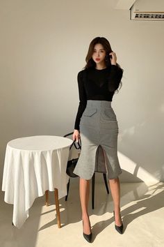Woman in a black top and pencil skirt with a slit, standing indoors