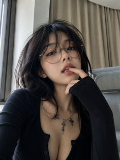 Woman with black hair and glasses wearing a black top and cross necklace