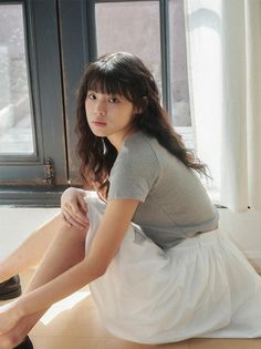 Woman with long wavy hair and bangs sitting on the floor by a window