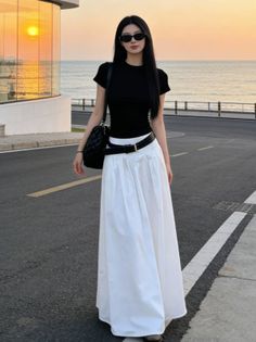 Woman in a black top and white skirt walking on a street at sunset