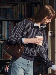 Woman in a striped shirt and jeans holding a cup in front of a bookcase