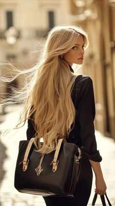 Woman with long blonde hair and a black shirt carrying a handbag outdoors