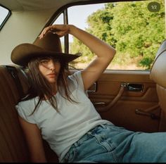 Woman in a cowboy hat and t-shirt sitting in a car with a green background
